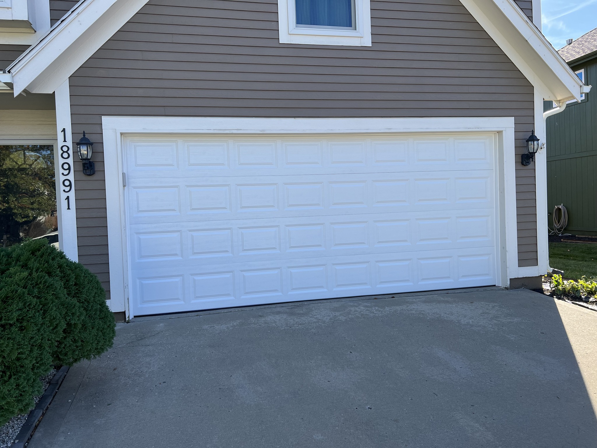 Exterior view of a newly installed Clopay 4050 garage door in white on a beige 2 story home.