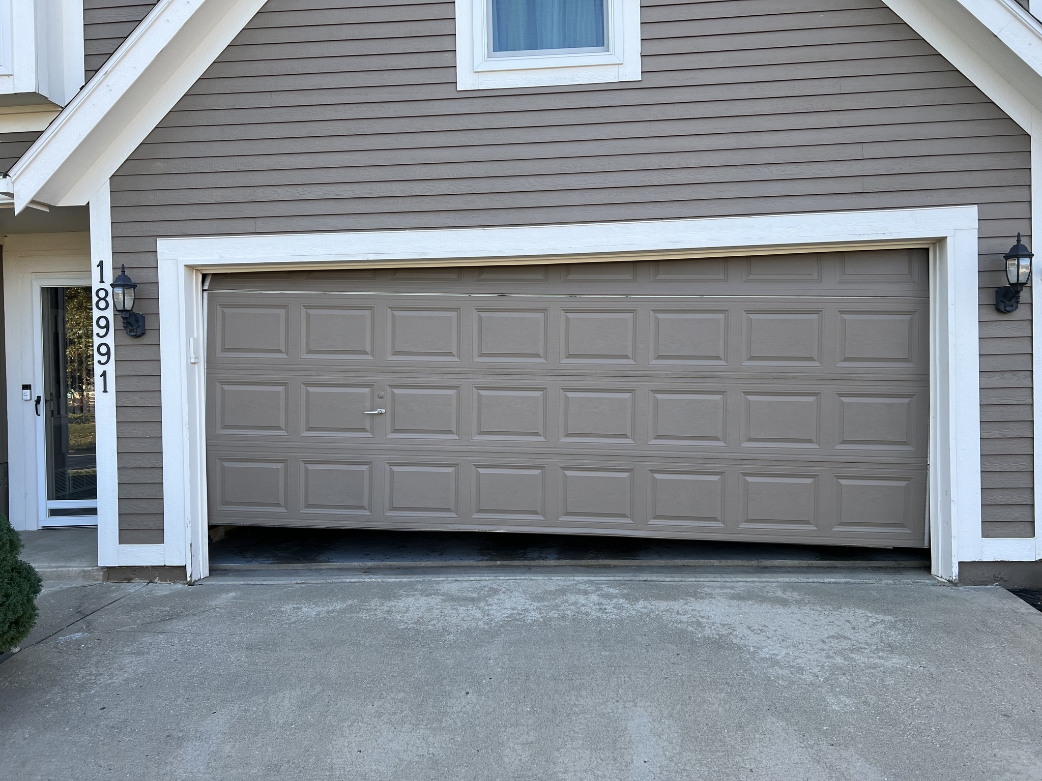 Exterior view of a beige house with a partially open garage door. One side is elevated due to a torsion cable snapping.