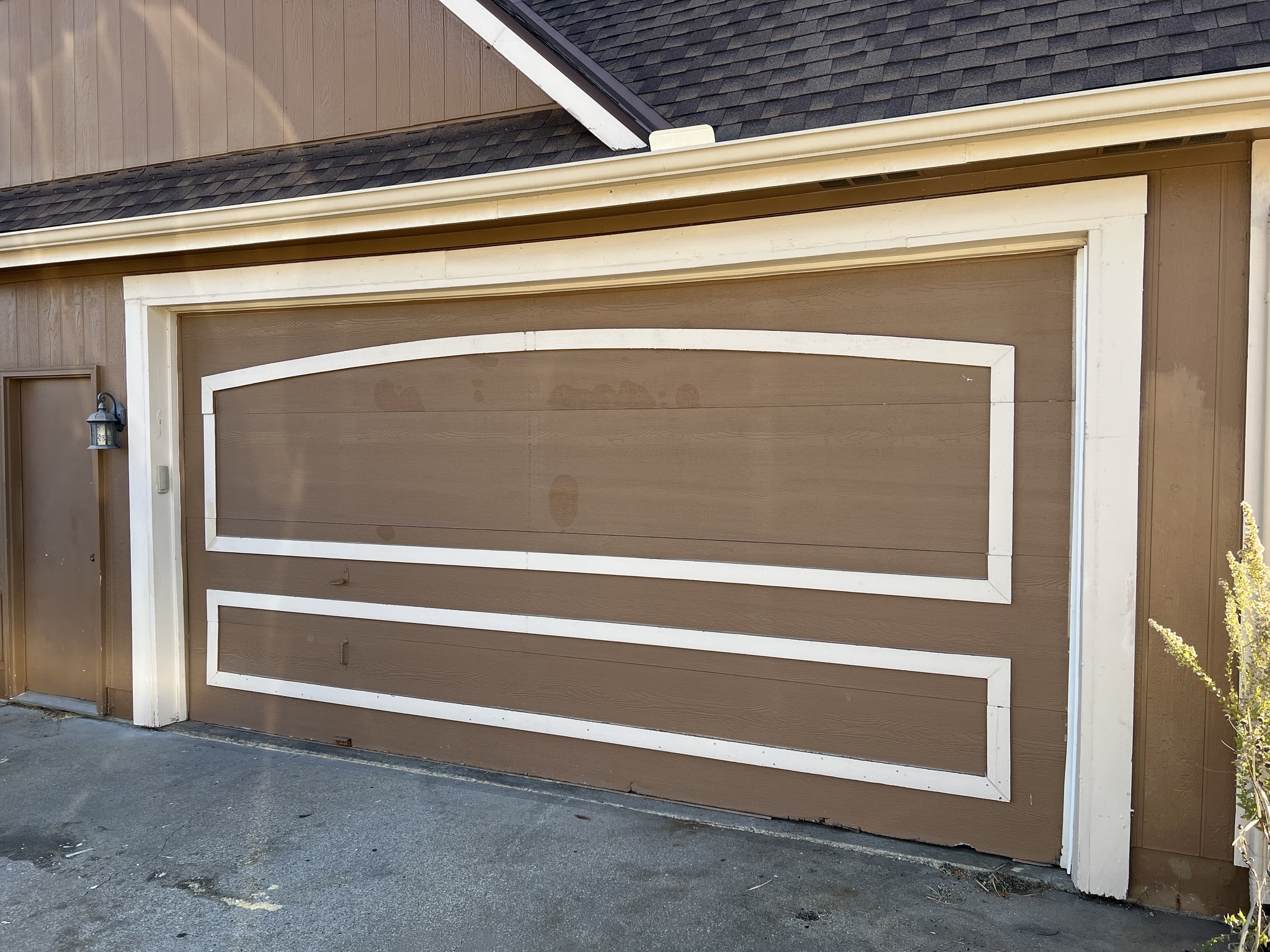 Brown garage door with white trim and geometric rectangular patterns, including signs of wear and stains.