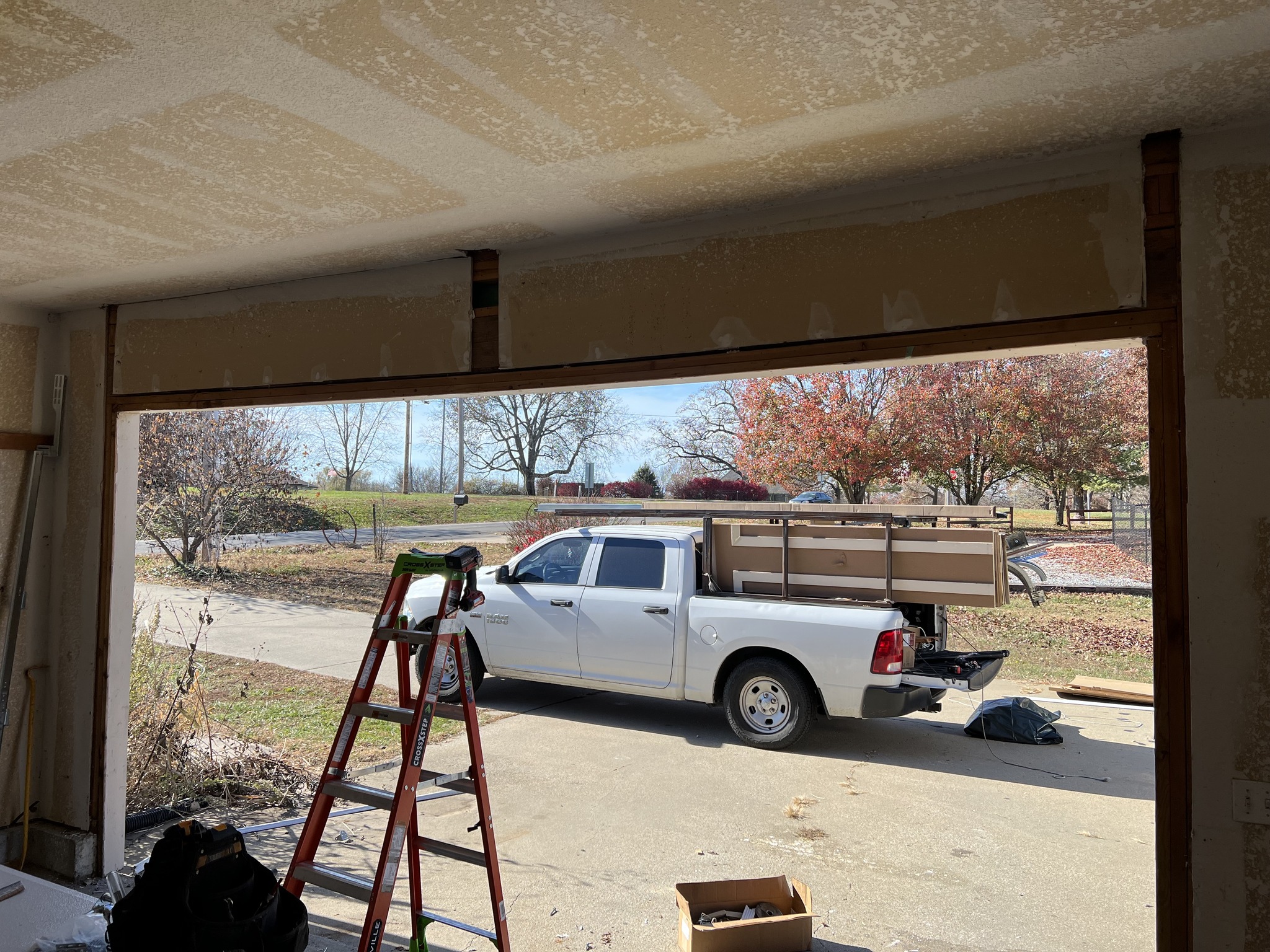 White pickup truck parked outside a garage under renovation with a red ladder and tools visible inside.
