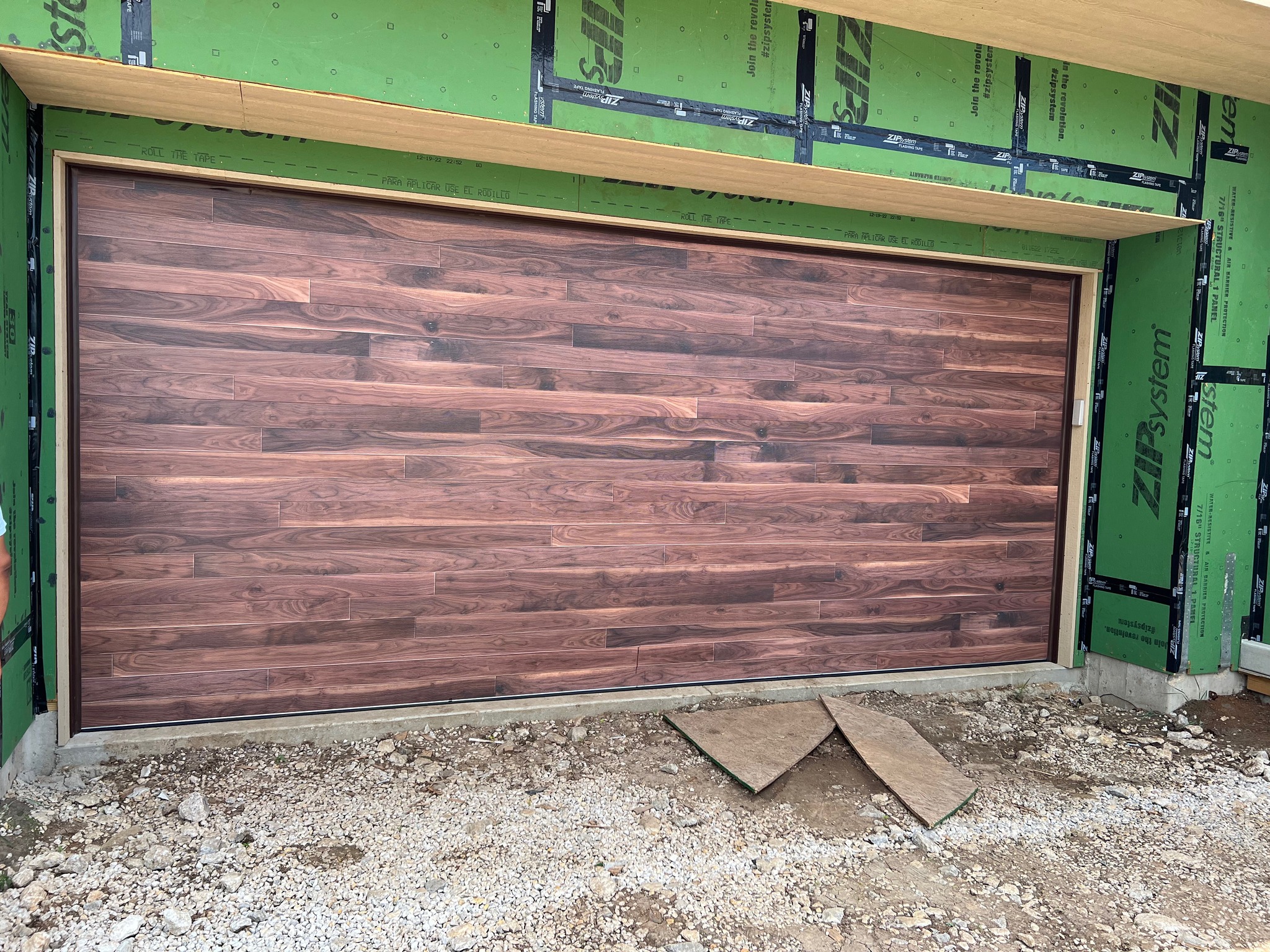 Exterior view of a newly installed 18x8 DoorLink 3700 in Walnut garage door with zip sheathing surrounding.
