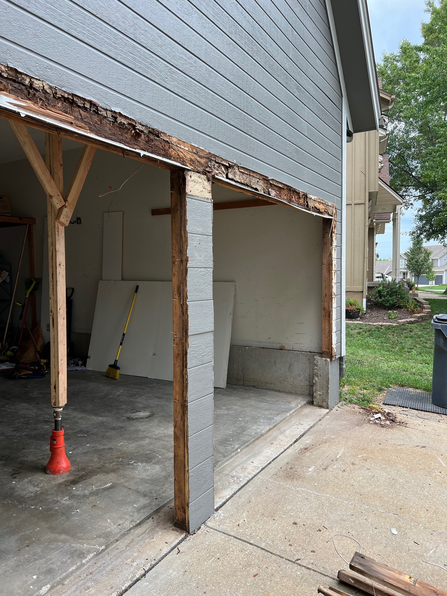 Partially demolished garage with rotted wooden frame exposed and a red jack supporting a wooden post.
