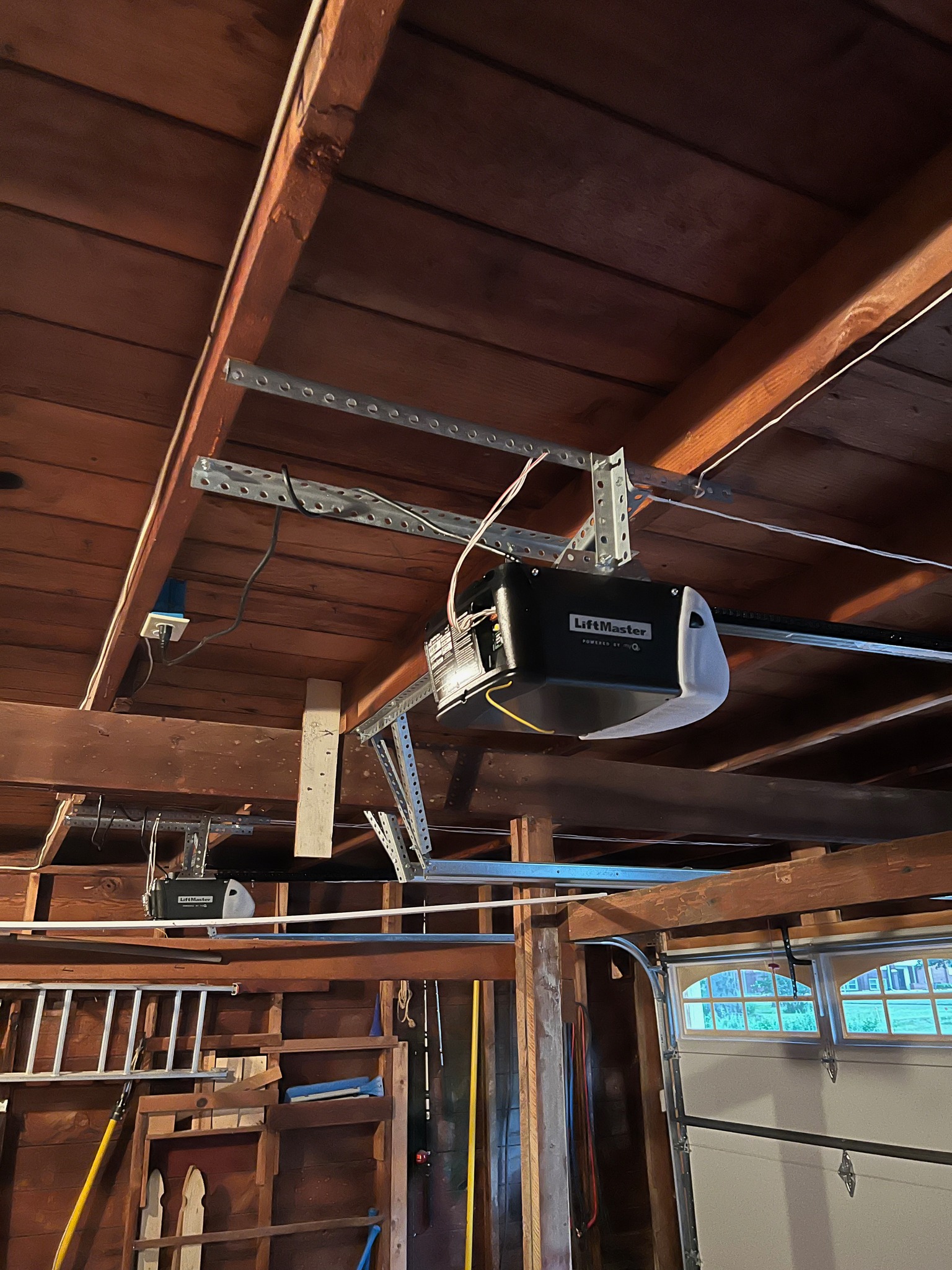 Garage ceiling with two LiftMaster 8165 garage door opener motors mounted on wooden beams and metal brackets.