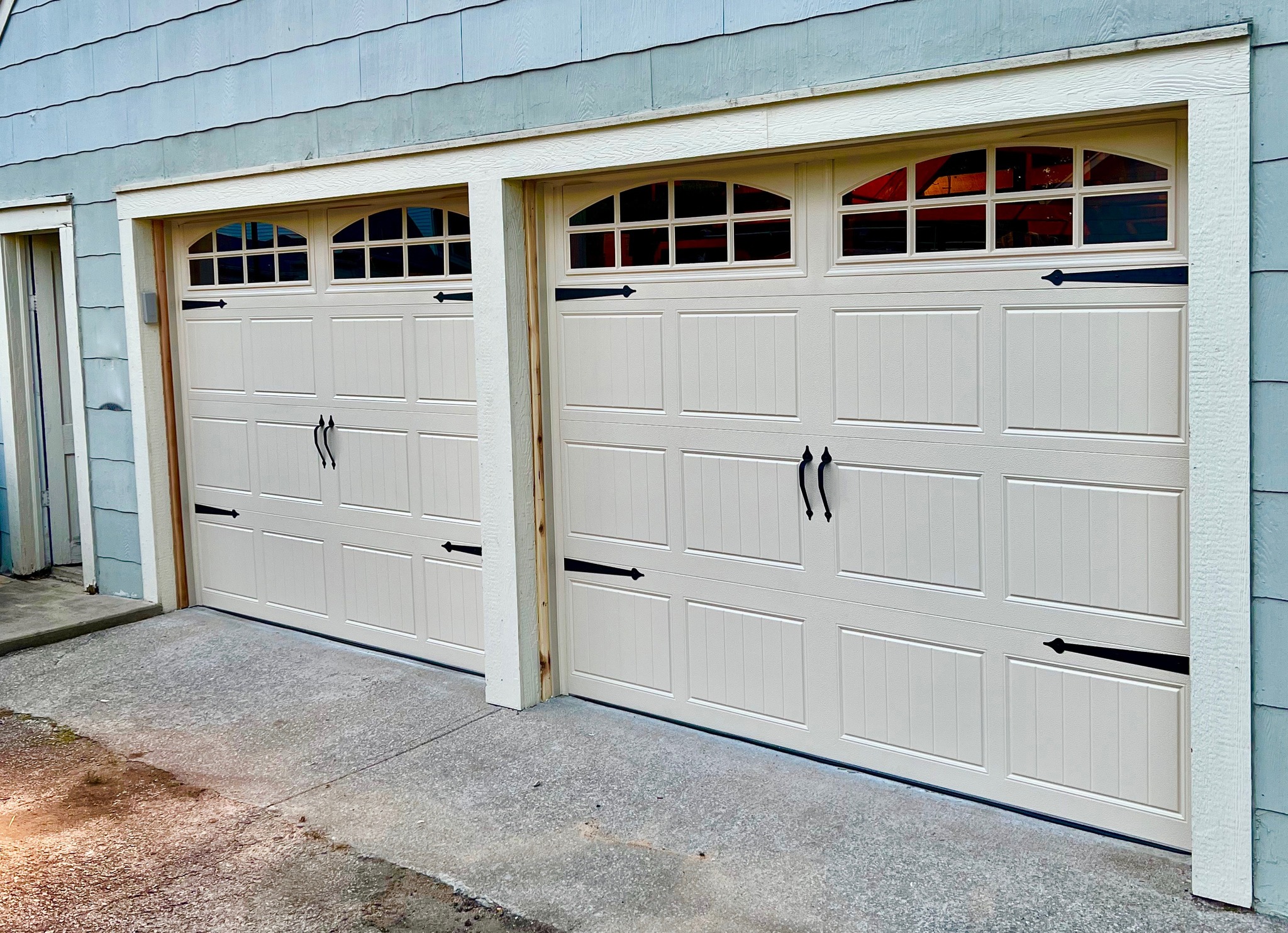 2 DoorLink 3630 steel garage doors in Almond. Long panel glass in top section with arched inserts. Doors have decorative hardware mounted on them.