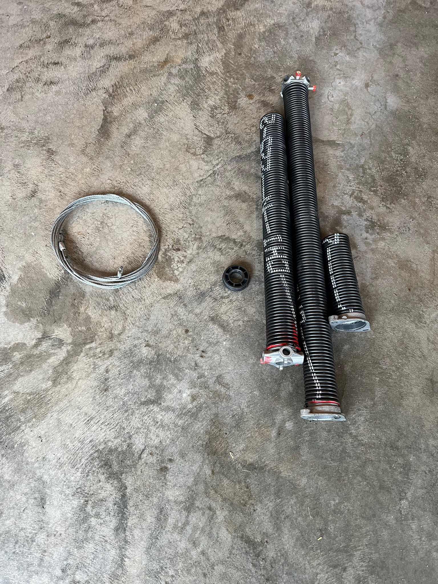 Garage door torsion cables and two black garage door torsion springs, 1 broken spring with center bearing on a concrete floor.