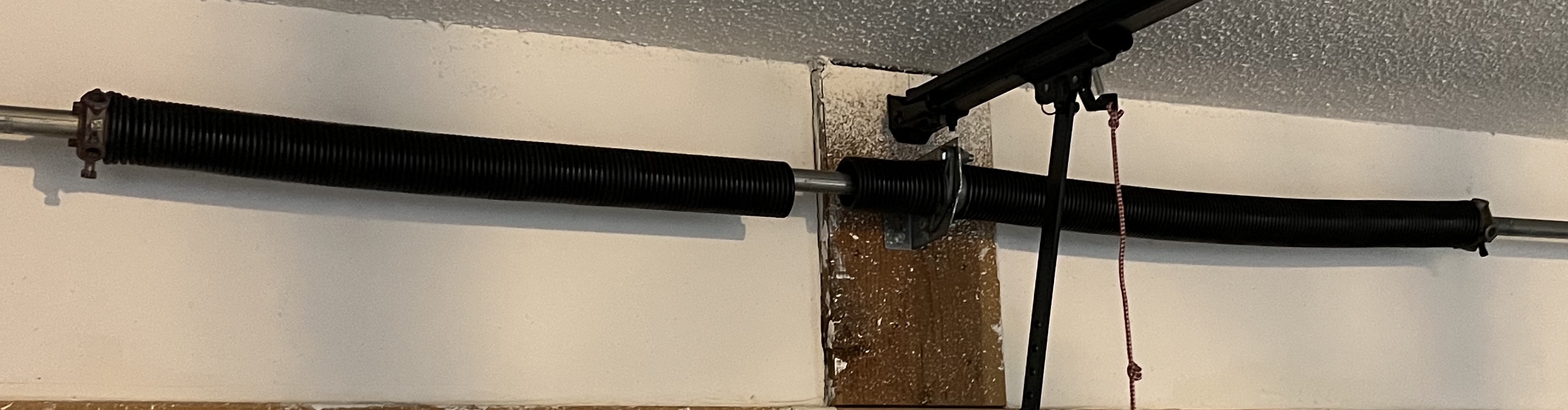 Broken garage door torsion spring mounted above the door frame on a wooden support beam.