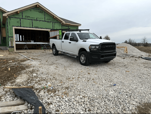 White RAM pickup truck parked on gravel in front of a house under construction with green ZIP System sheathing.