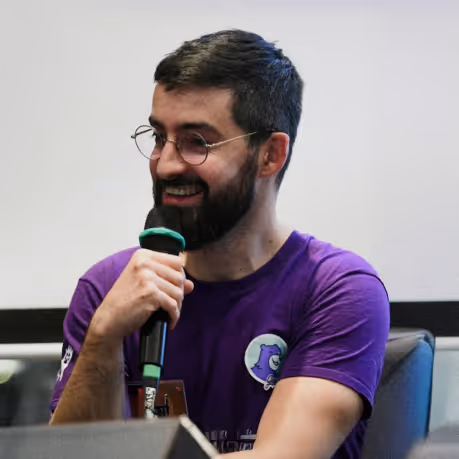 Homme avec barbe et lunettes tenant un microphone et souriant lors d'une conférence.