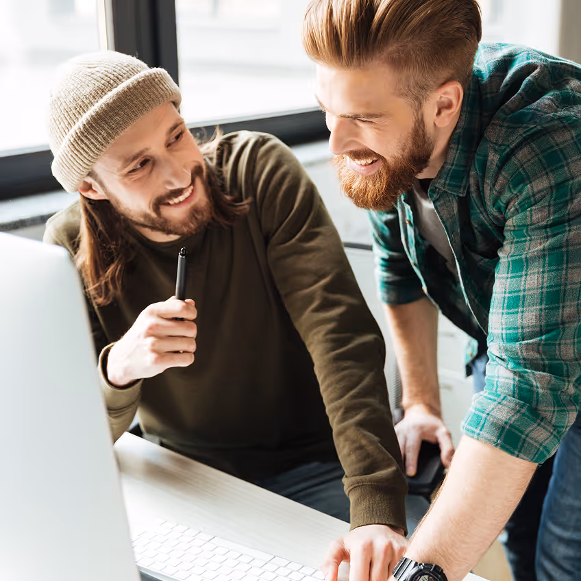 Deux hommes souriants collaborent devant un ordinateur dans un bureau lumineux.