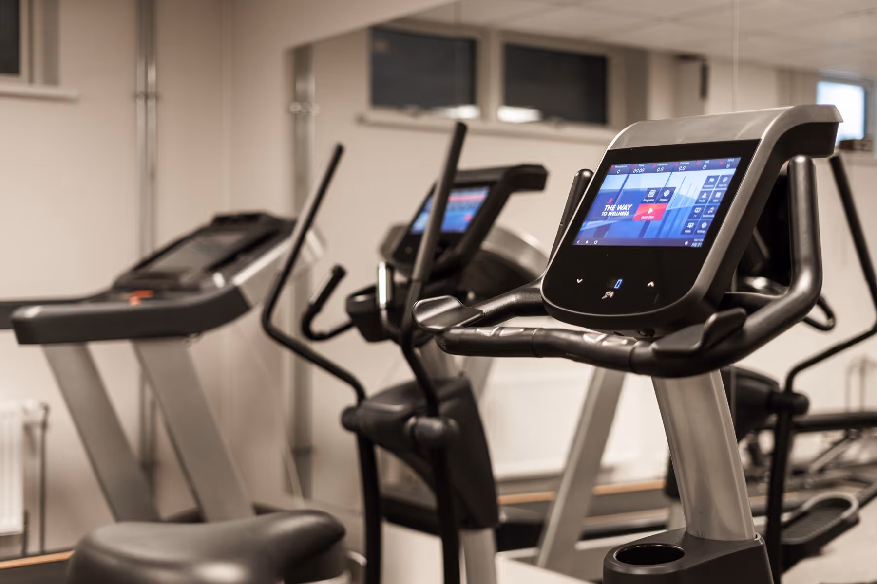 Close-up of a modern stationary bike and treadmill with digital screens in a home gym room.