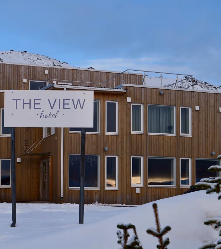 Snow-covered ground in front of a wooden hotel building with a sign reading 'THE VIEW hotel' against a blue sky.