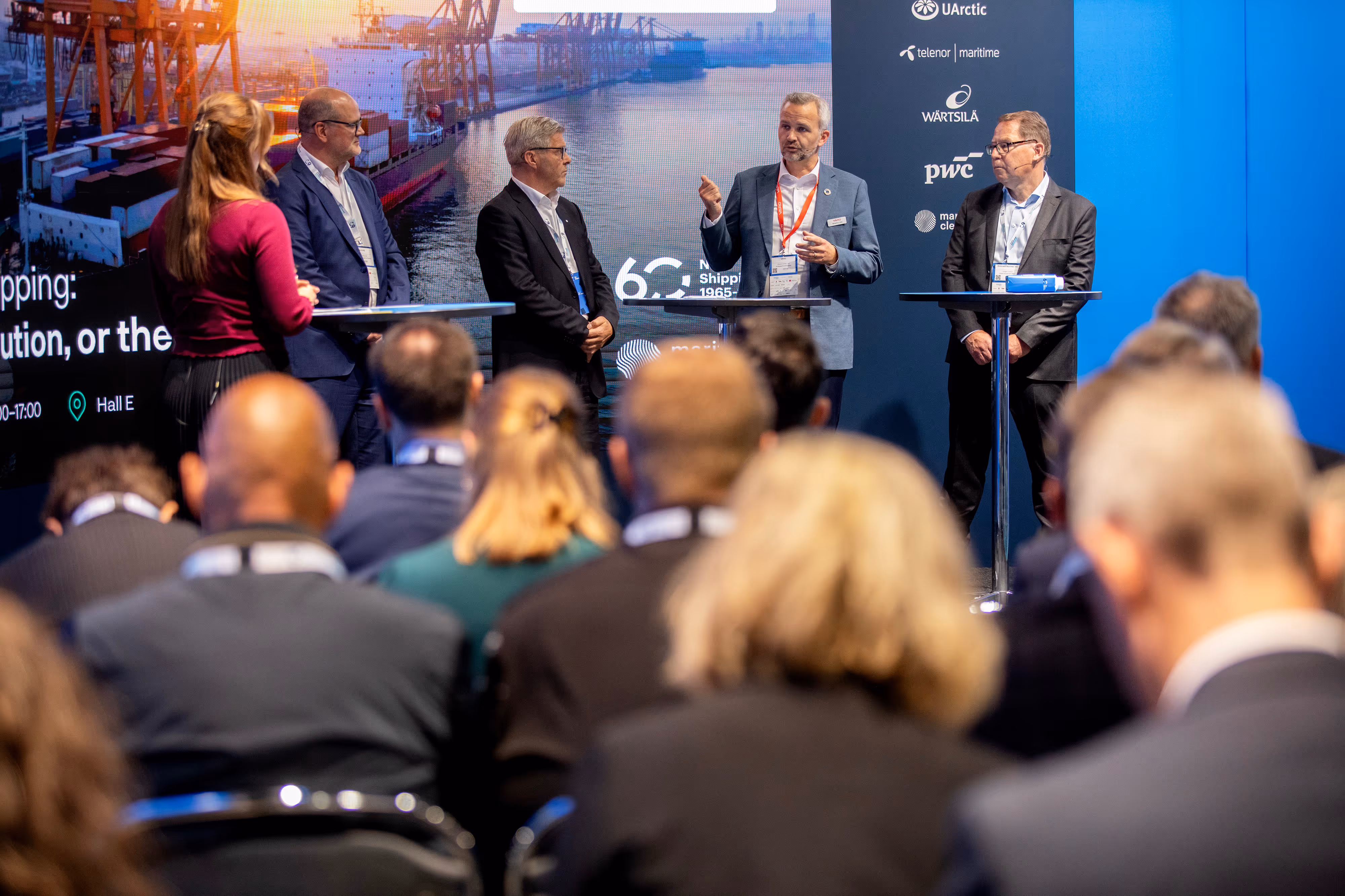 Panel of five professionals in suits presenting at a maritime conference with seated audience.