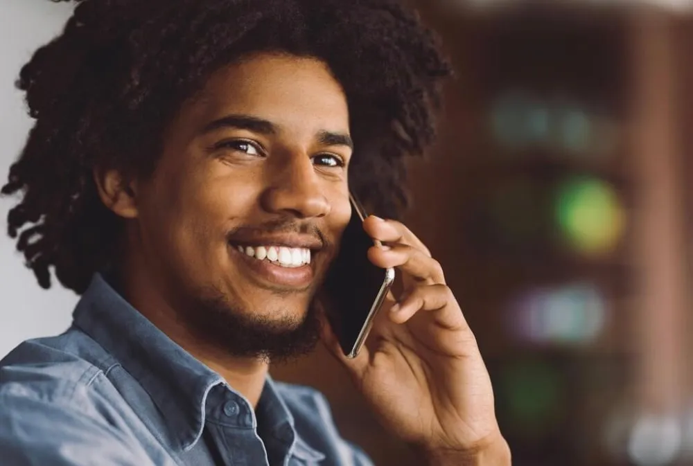 Smiling young man with curly hair talking on a smartphone.