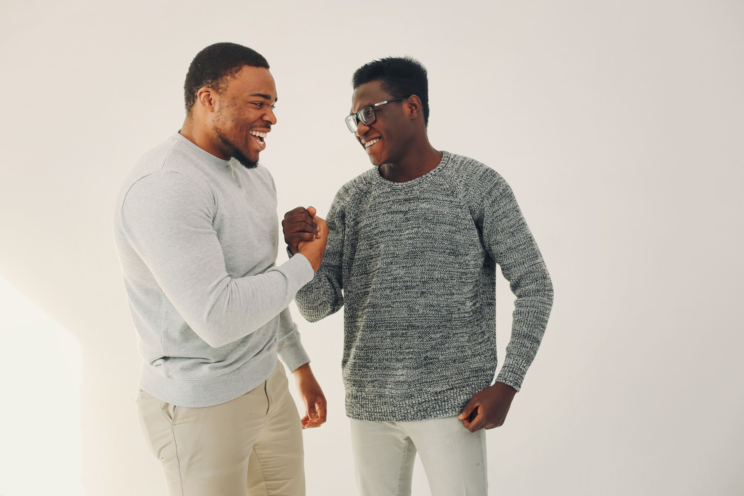 Two men smiling and clasping hands in a friendly gesture against a plain light background.