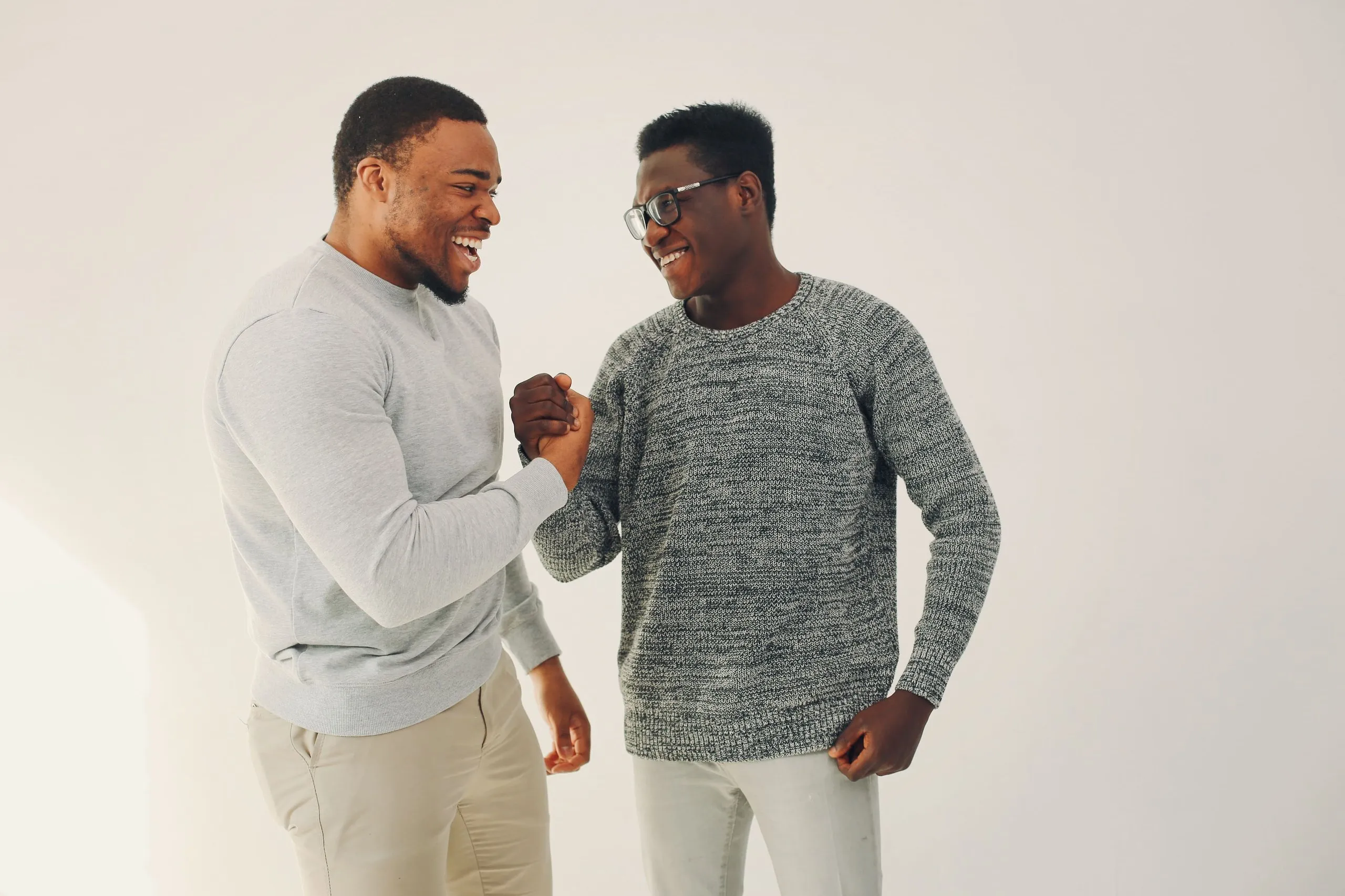 Two men smiling and clasping hands in a friendly gesture against a plain light background.
