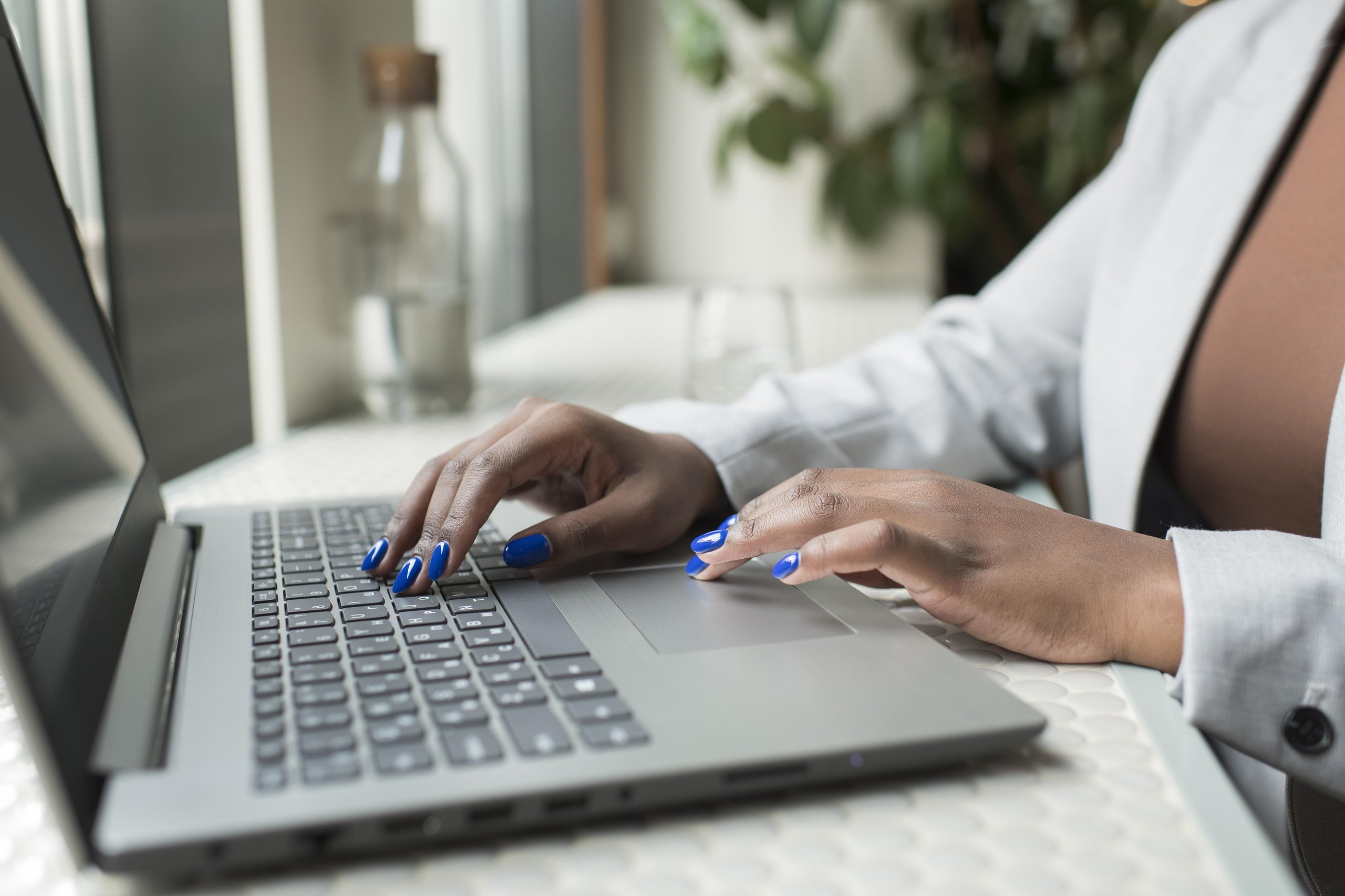 Person with blue nail polish typing on a laptop keyboard at a white table.