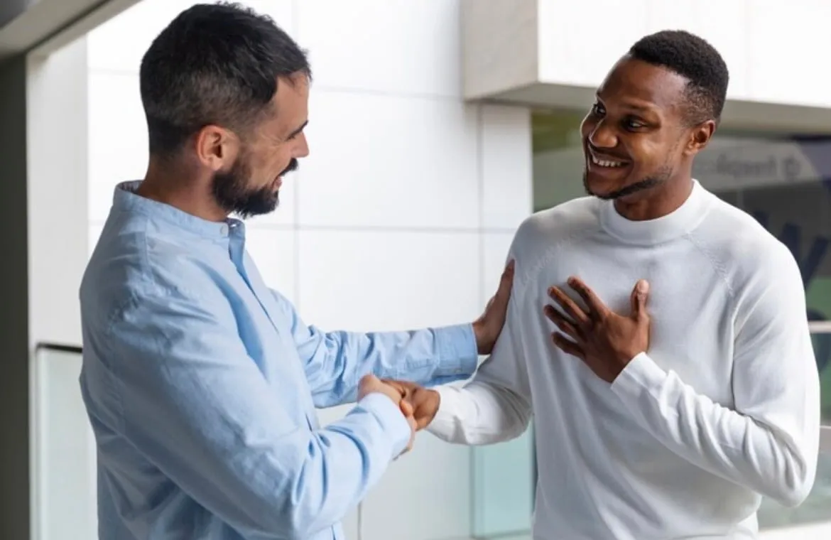 Two men smiling while shaking hands, one with a hand on the other's shoulder in a friendly gesture.