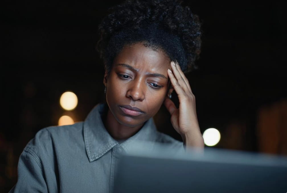 Young woman looking at a laptop screen with a concerned expression, resting her head on her hand.