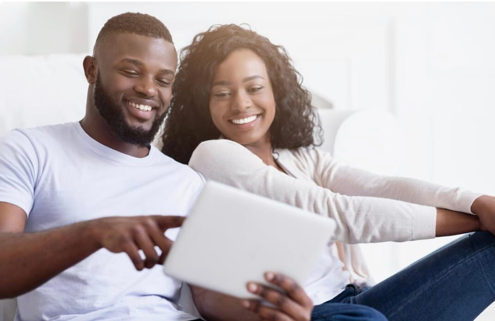 Smiling man and woman sitting together on a couch looking at a tablet.