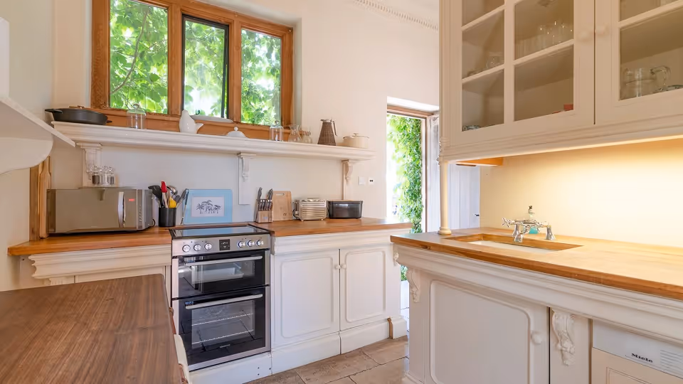 Bright kitchen with wooden countertops, white cabinetry, a stove, microwave, and a window showing green foliage outside.