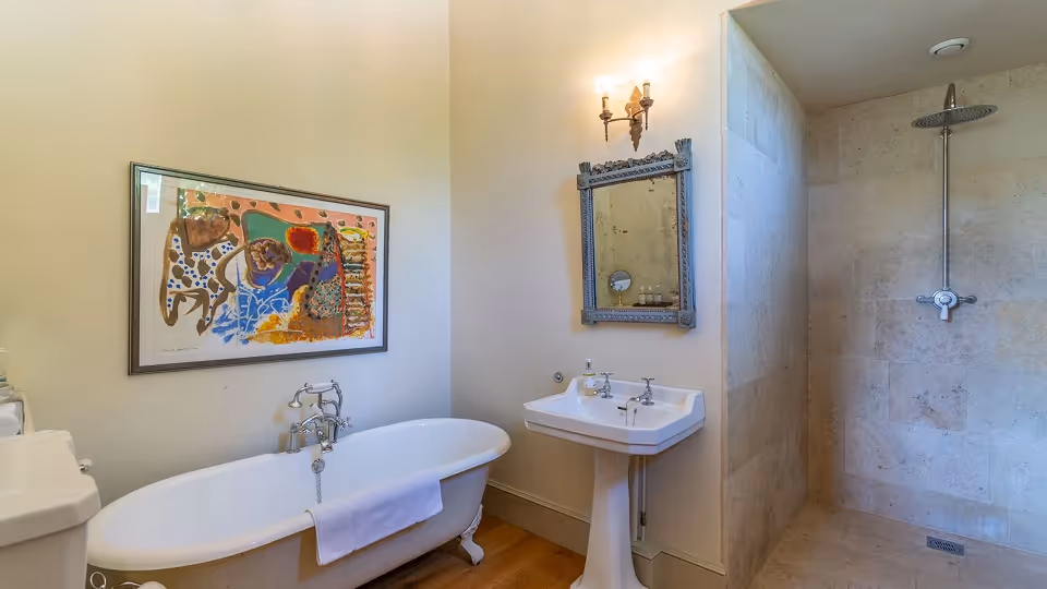 Bathroom with a clawfoot bathtub, a pedestal sink with a framed mirror above, and a tiled walk-in shower.