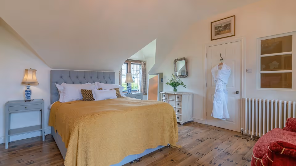 Formal garden with a stone-edged pond, manicured hedges, flowering plants in large pots, and historic stone buildings under a blue sky.