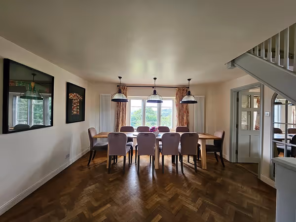 Modern dining room with eight upholstered chairs around a wooden table under three pendant lights, a window with curtains, and wooden parquet flooring.