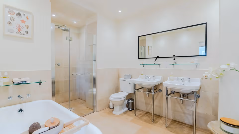 Bright modern bathroom with double sinks, glass-enclosed shower, toilet, and freestanding bathtub with bath accessories.