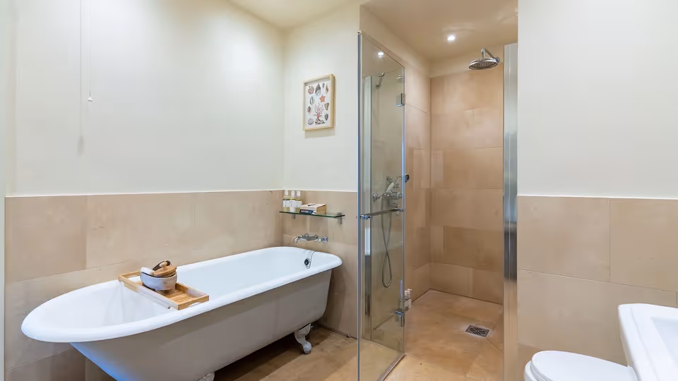 Modern bathroom with a white clawfoot bathtub, a wooden bath tray, glass-enclosed shower, and beige tiled walls.