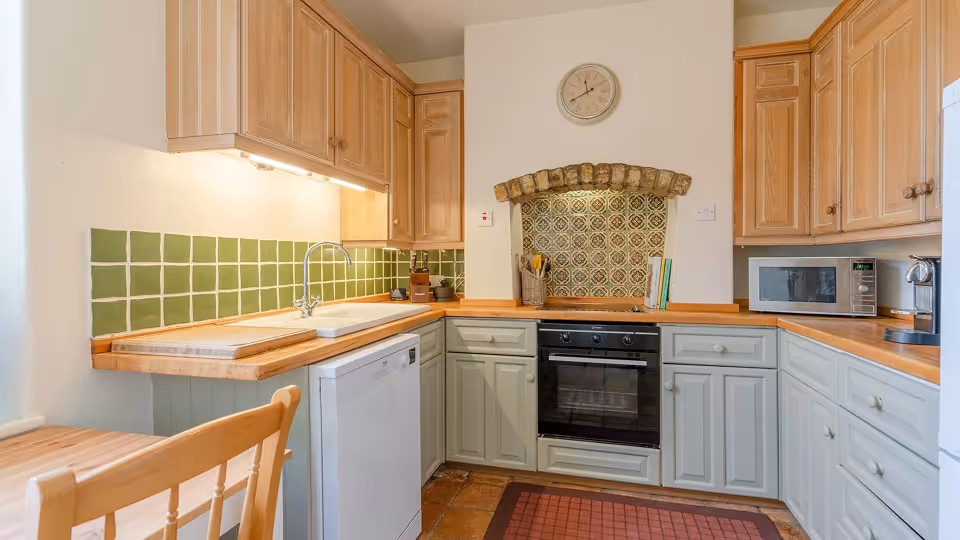 Cozy kitchen with wooden countertops, green tile backsplash, oven, microwave, and a wooden chair in foreground.