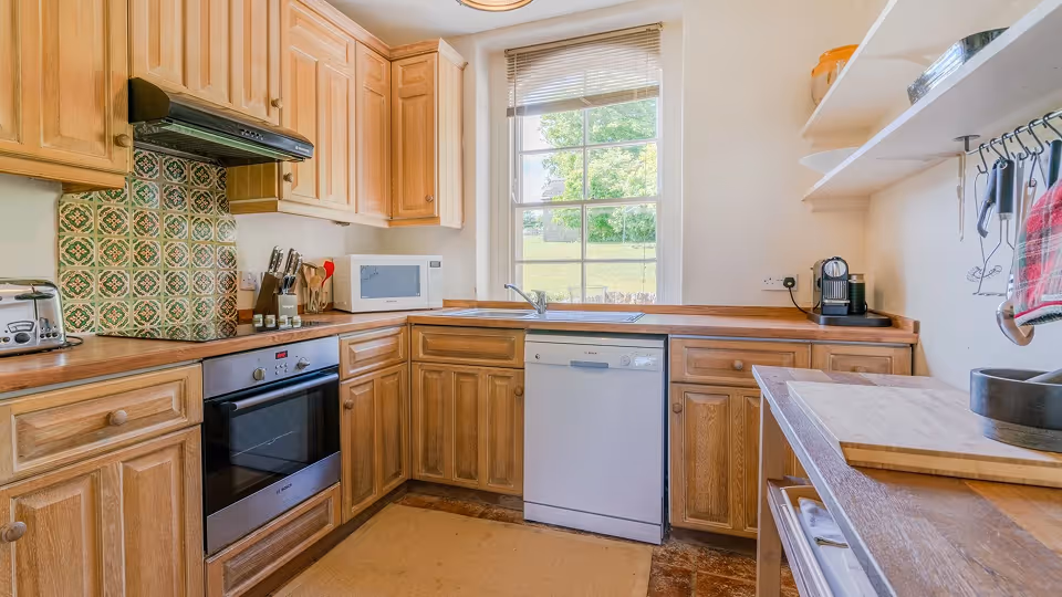 Cozy kitchen with wooden cabinets, dishwasher, oven, microwave, toaster, and a window overlooking a garden.