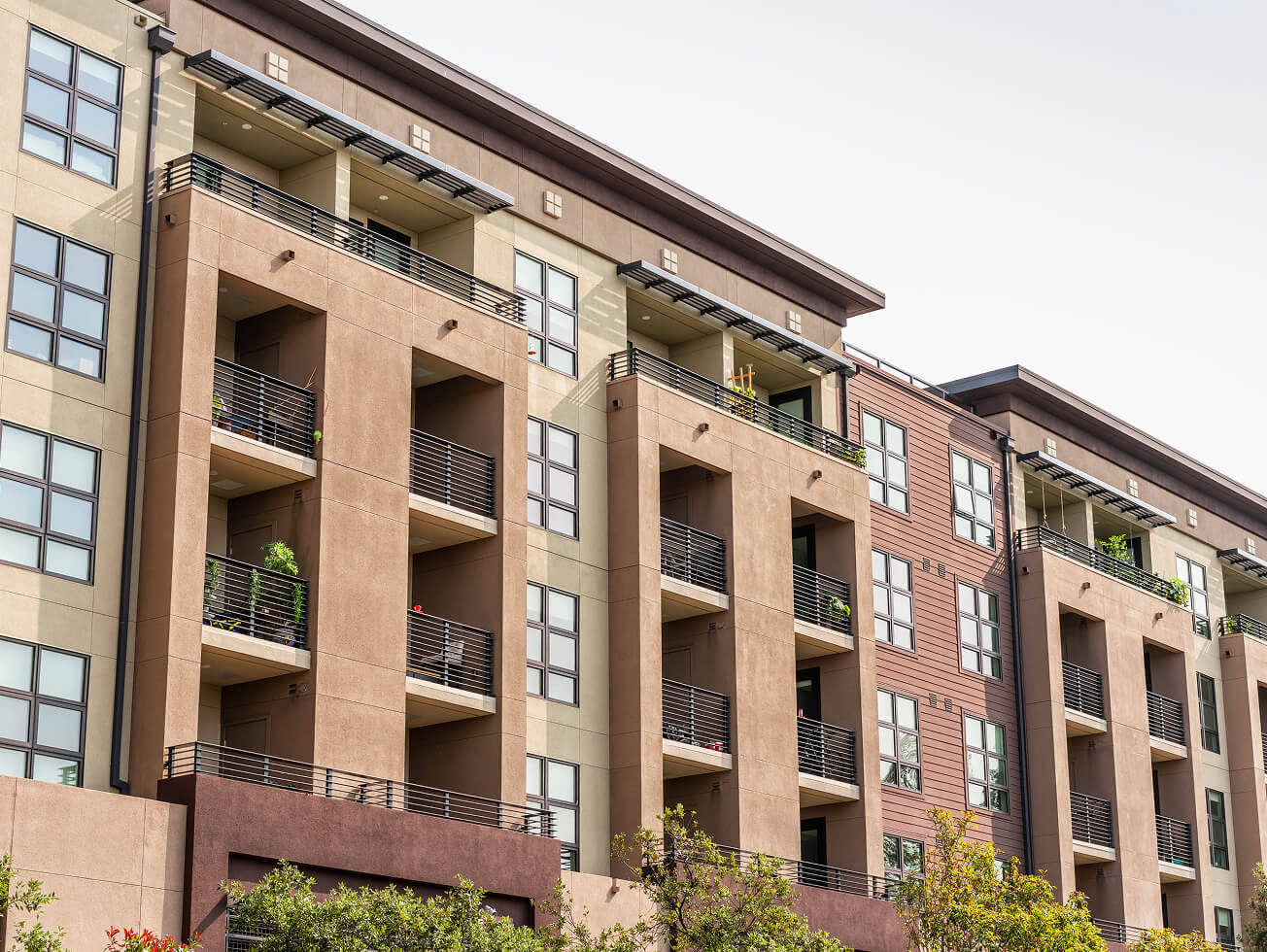 Modern apartment building with multiple floors, featuring balconies with plants.