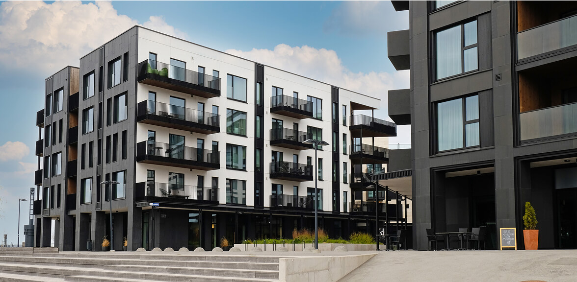 Modern apartment buildings with large windows and balconies are seen under a blue sky.