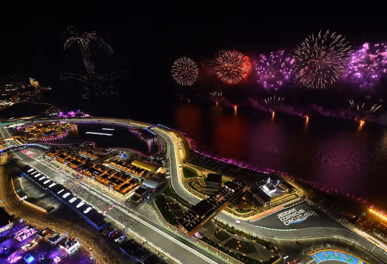 Aerial night view of Jeddah Corniche Circuit with fireworks illuminating the sky and reflected in the water.