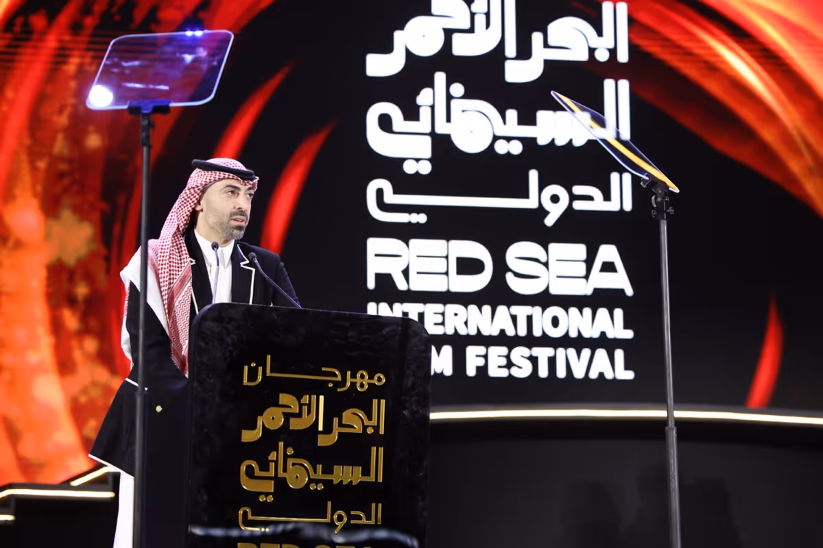 A man in traditional Middle Eastern attire speaking at a podium at the Red Sea International Film Festival.