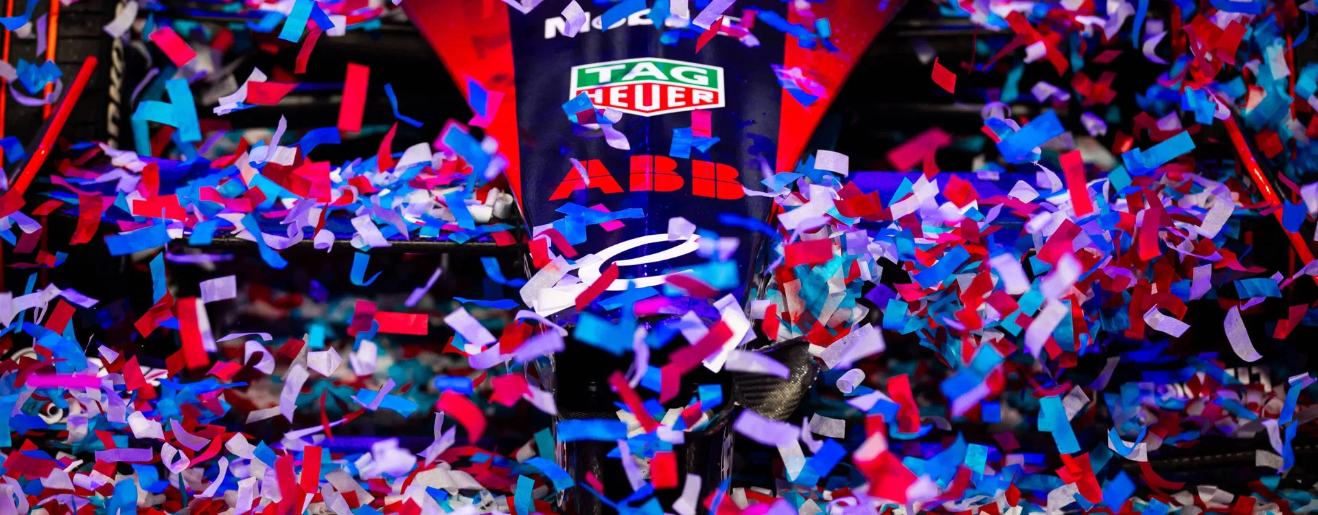 Close-up of a red and black Formula E car covered in blue, red, and white confetti.