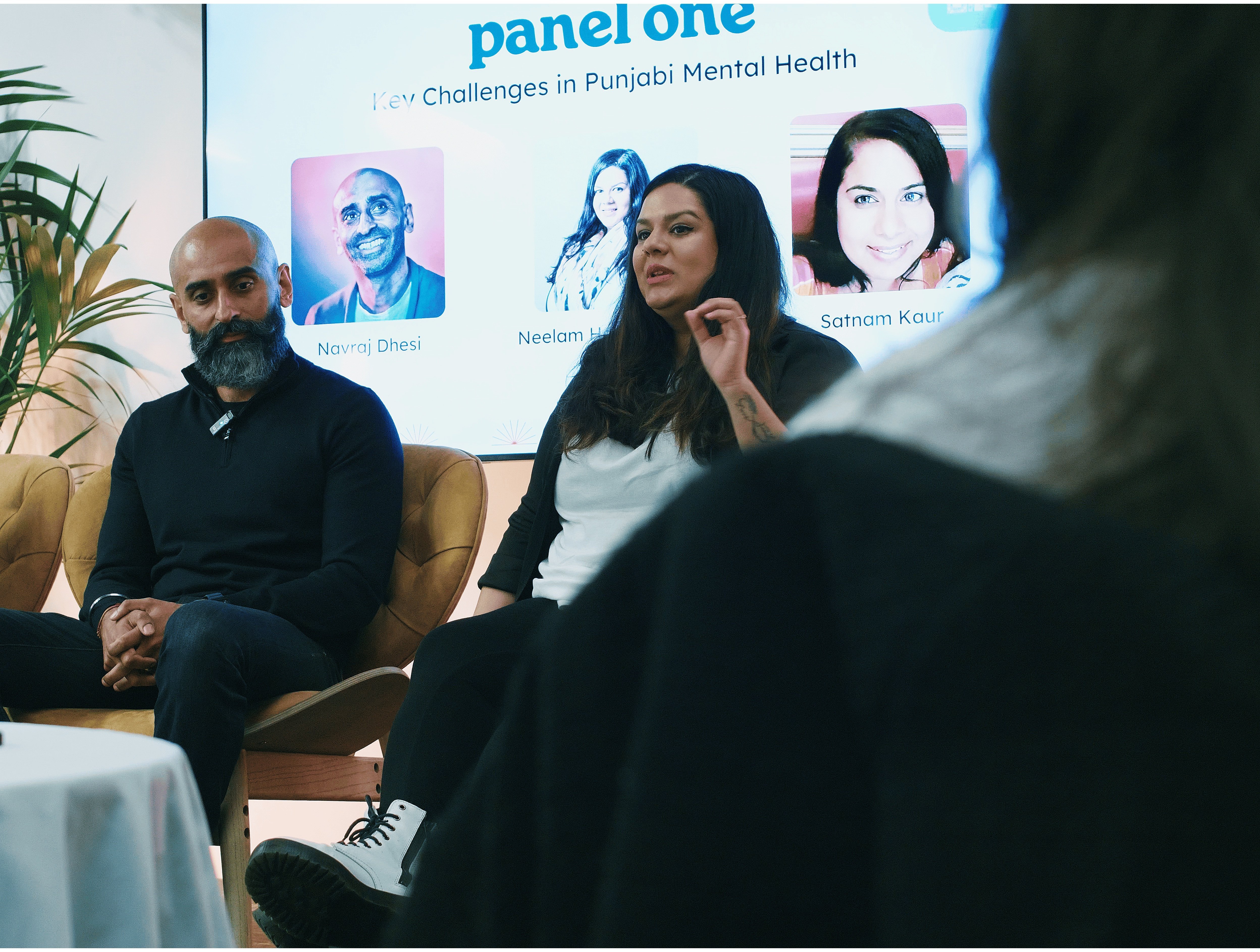 Two panel speakers, a man with a beard and a woman with long dark hair, seated and discussing mental health with an audience visible in the foreground.