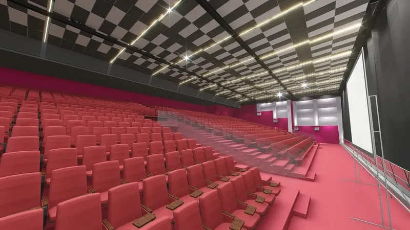 Modern auditorium with tiered red seats facing a large blank projection screen and a checkered ceiling.