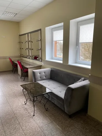 Room with gray cushioned sofa, glass coffee table, red chairs, mirrors, and two windows with blinds.