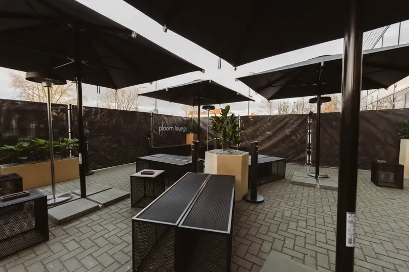 Outdoor lounge area with black benches, tables, umbrellas, and planters on a brick patio.