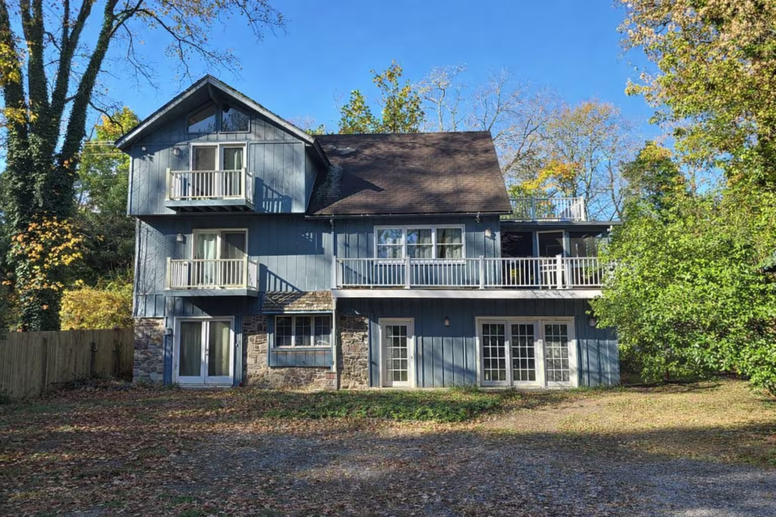 Three-story blue house in New Hope, Pennsylvania with stone accents, multiple balconies, and surrounded by trees under a clear blue sky.