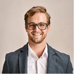 Porträt eines lächelnden Mannes mit Brille und Sakko vor neutralem Hintergrund.