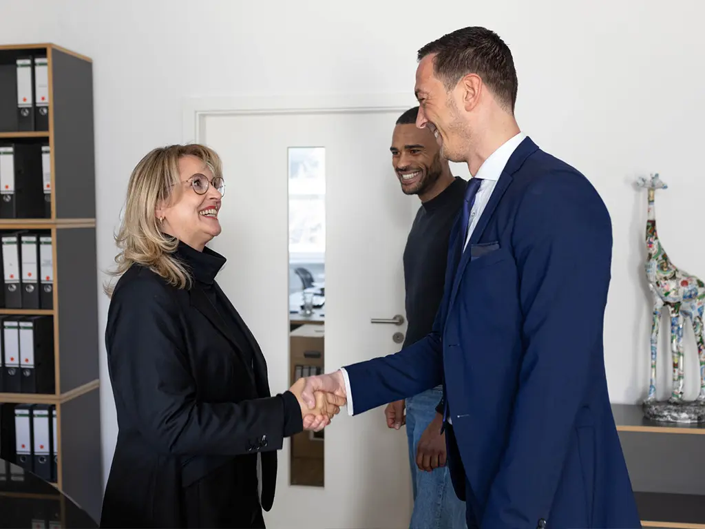 Nicole Flockenhaus begrüßt zwei Kunden mit einem Händedruck, sie treffen sich zu einem geschäftlichen Austausch