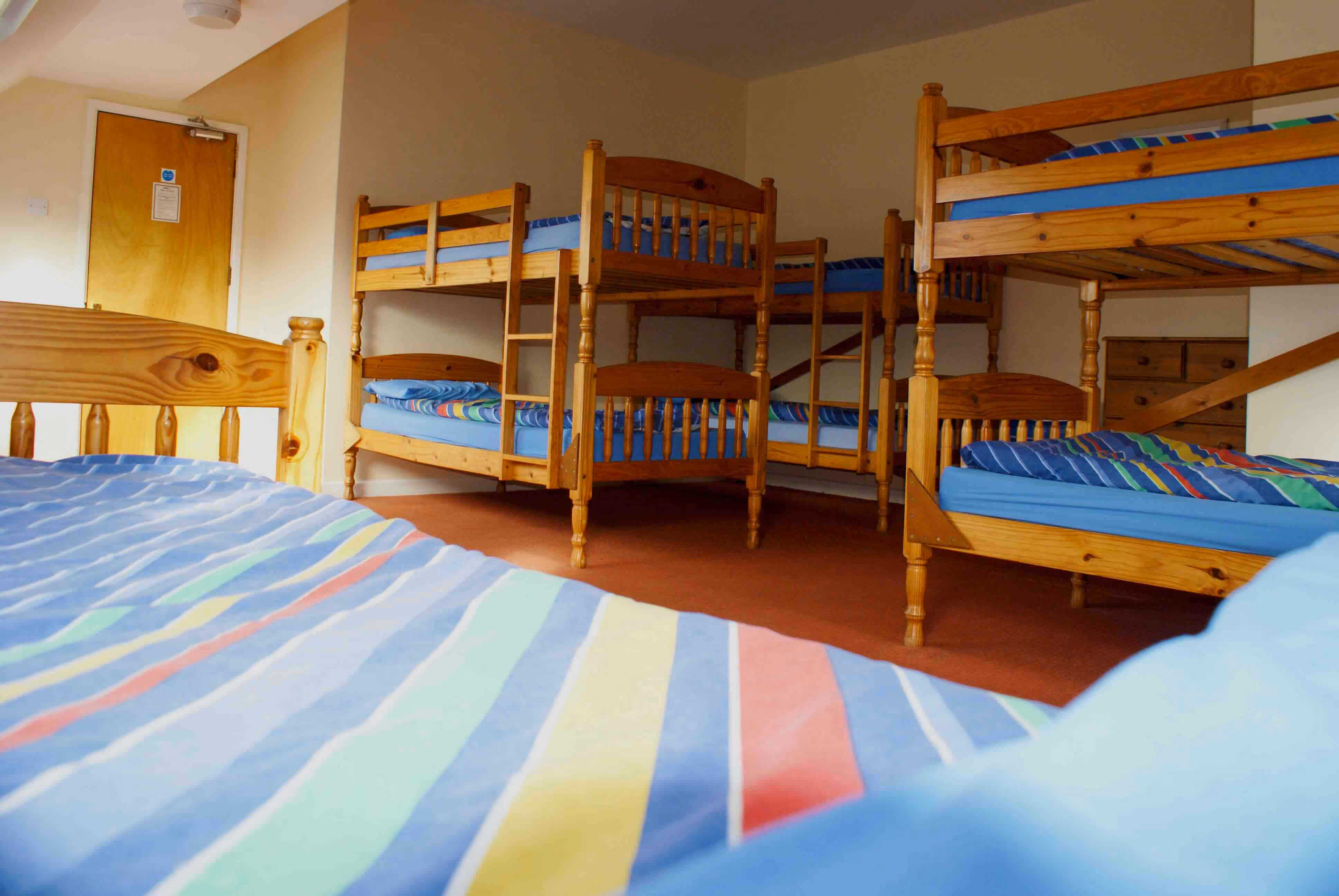 Dormitory room with multiple wooden bunk beds and colourful striped bedding.