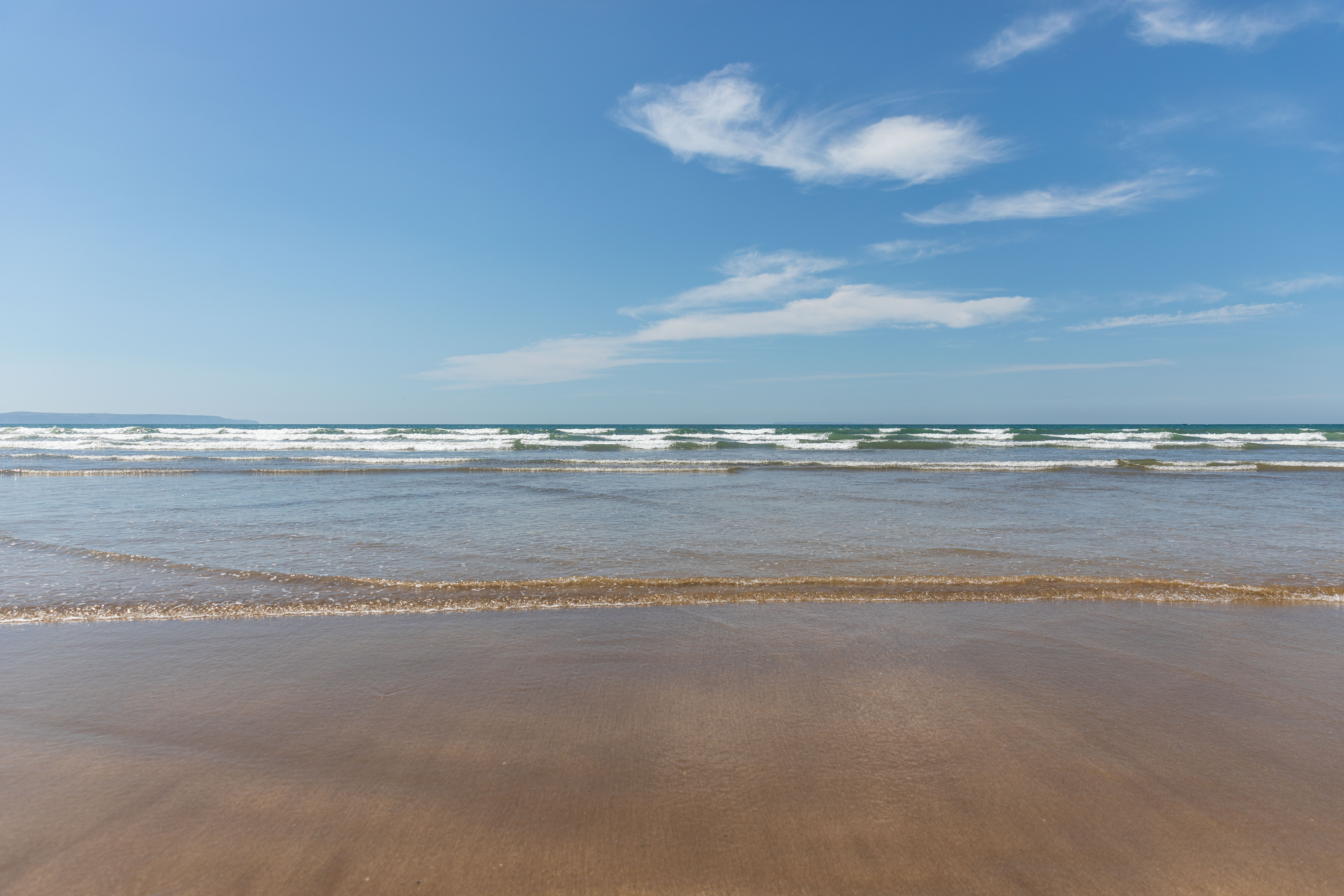Calm beach with gentle waves under a clear blue sky with a few scattered clouds.