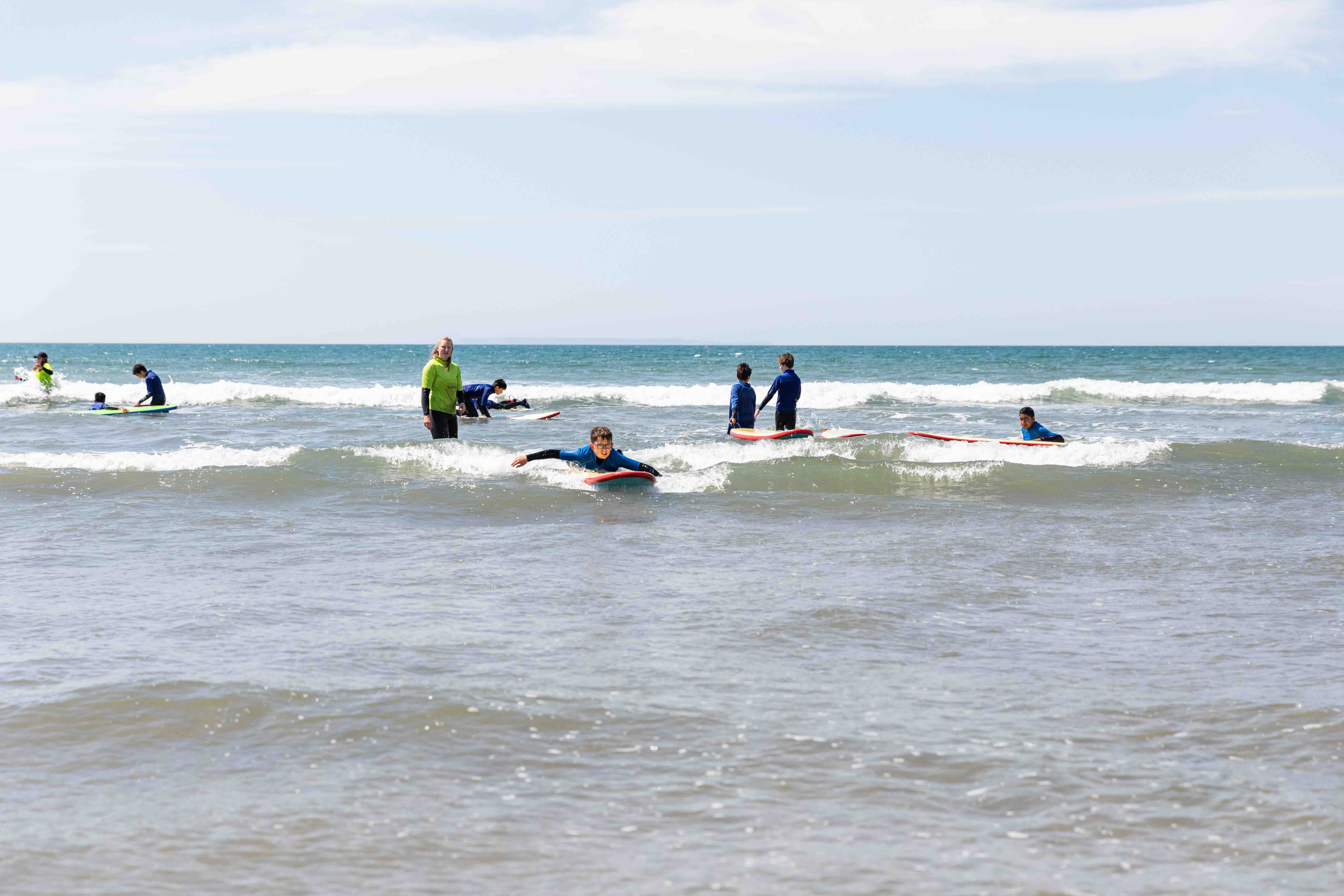 Children learning to bodyboard in the ocean with an instructor standing in the water.
