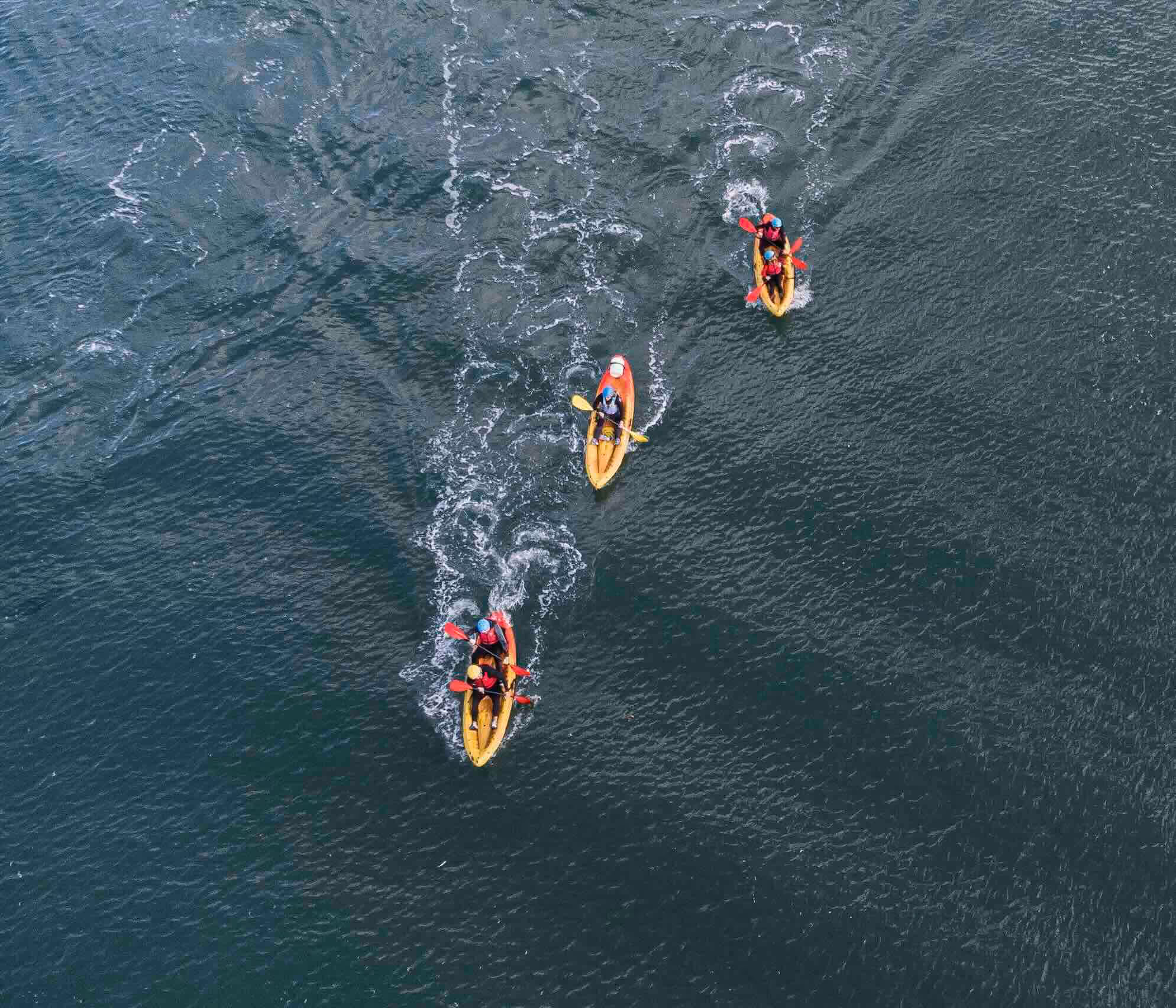 Aerial view of three kayaks with paddlers moving through rippling water.