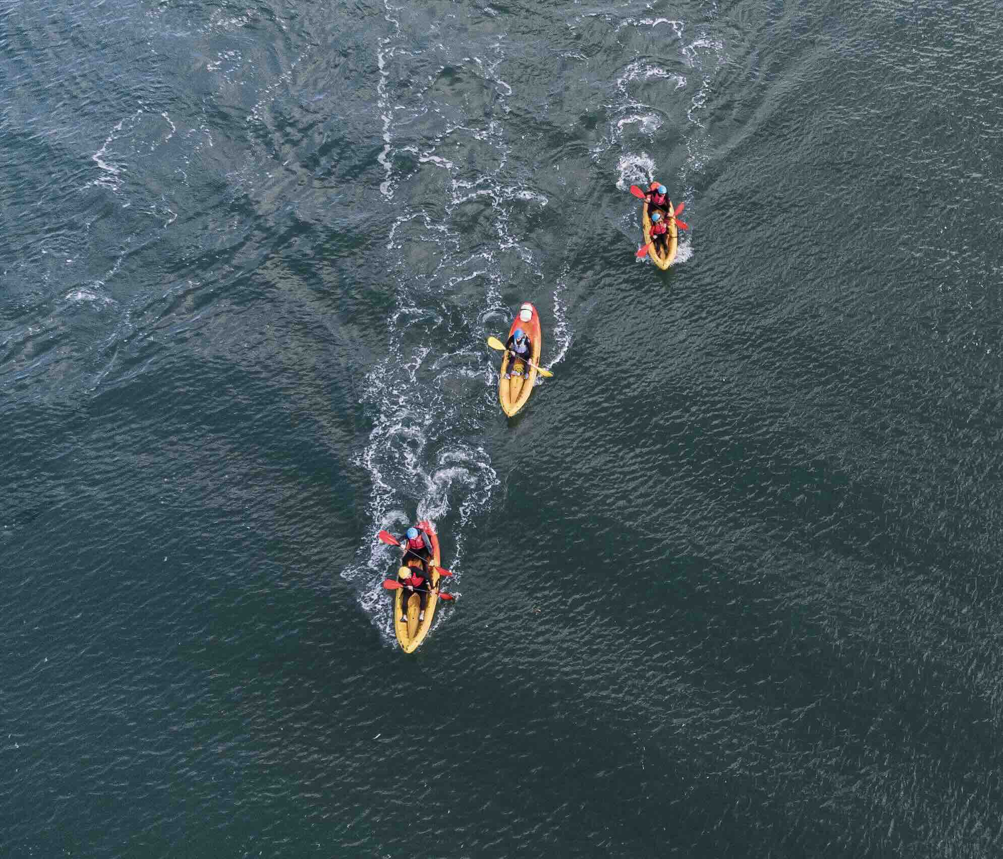 Aerial view of three kayaks with paddlers moving through rippling water.