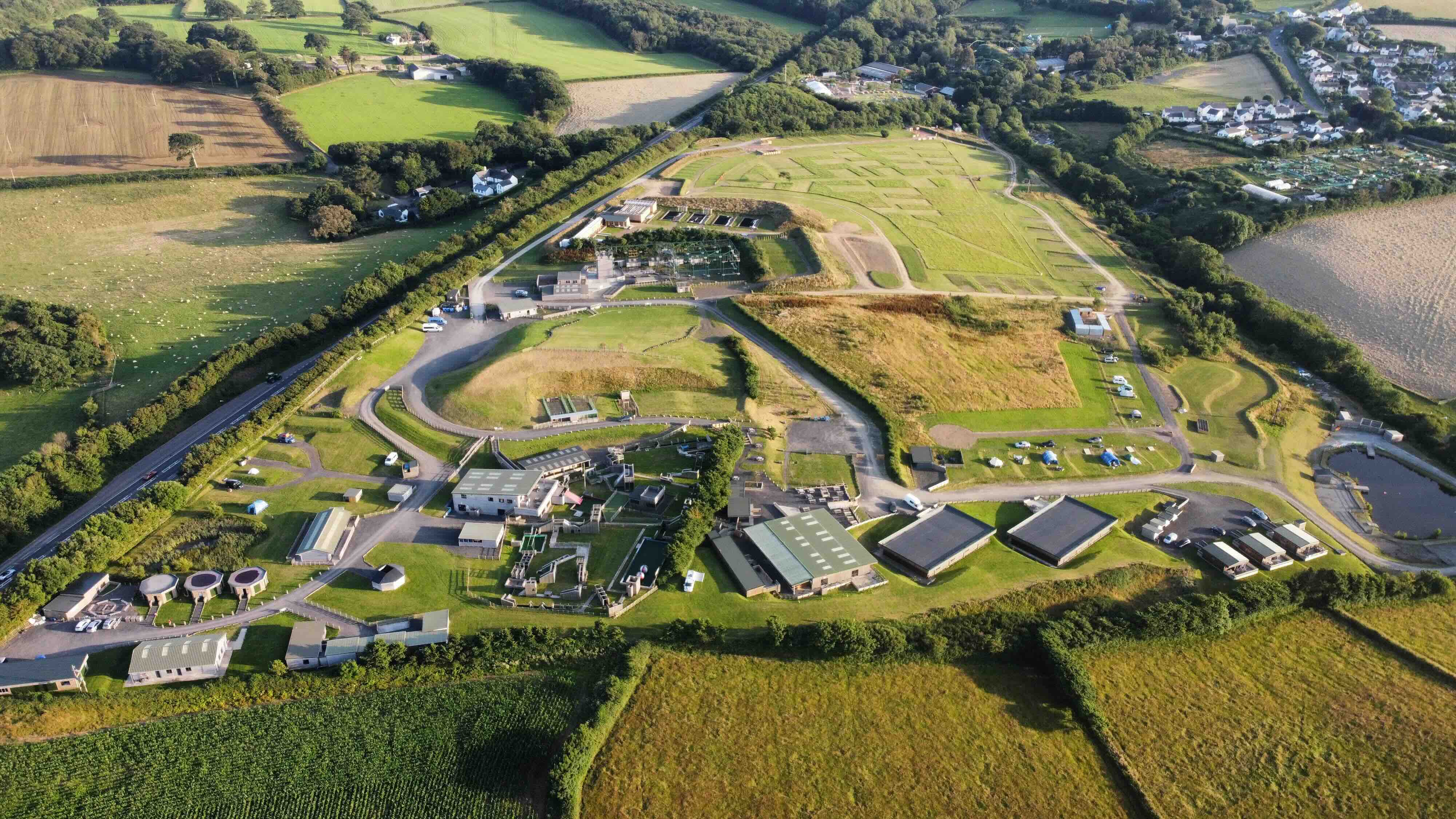 Aerial view of an industrial or utility complex surrounded by green fields, roads, and scattered buildings in a rural area.