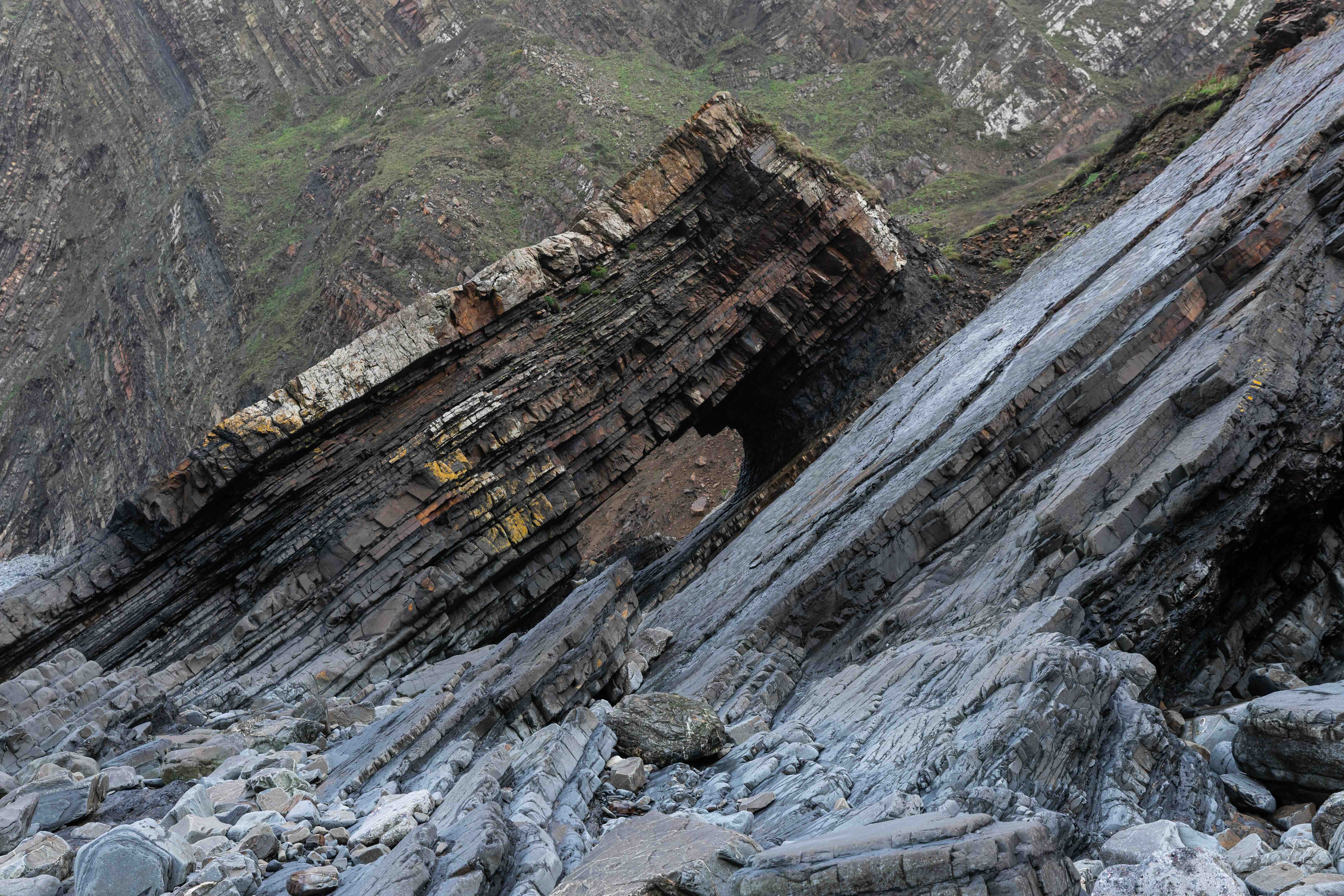 Rock formation with a natural arch and layered geological strata on a rocky shore.